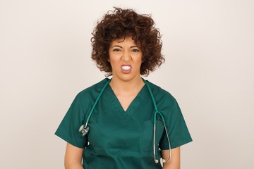 Mad crazy doctor woman clenches teeth angrily, being annoyed with coming noise, dressed in medical uniform, isolated over gray background. Negative feeling concept.