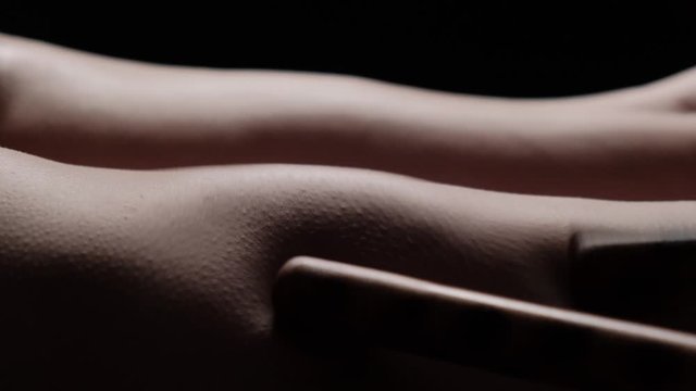 Female body massage with bamboo sticks on a black background. Slow motion. Leather close-up.