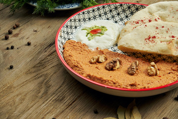 Muhammara is a classic eastren dish. baked pepper and walnut puree with Bazlama and yogurt in a ceramic plate on a wooden background.