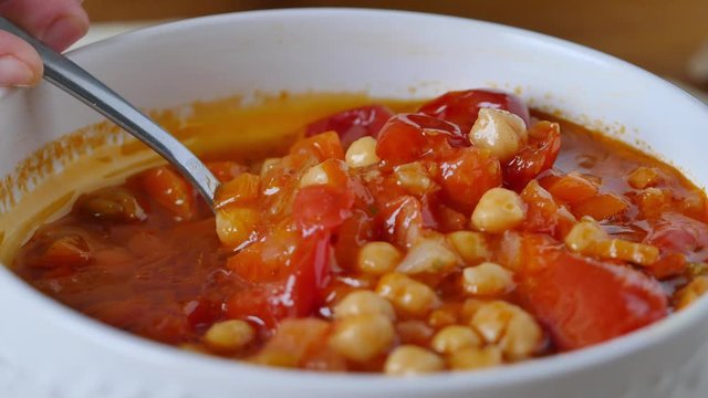 Healthy eating, take tablespoon chickpeas soup with tomatoes in a bowl. On the table a bowl of creamy and rustic legume soup. Eating healthy vegetarian dinner. Cozy and warm food. Protein dinner. 