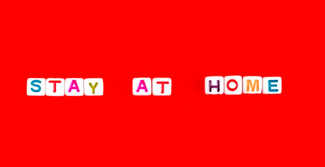 Phrase Stay At Home made out of colorful beads on red background, flatlay, top view
