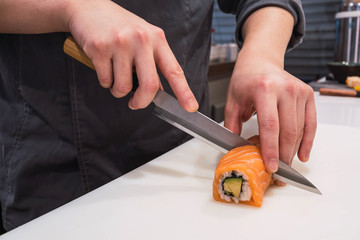 Detail of the hands of a chef cutting pieces of salmon sushi with rice with a knife on top of a wood © Marc