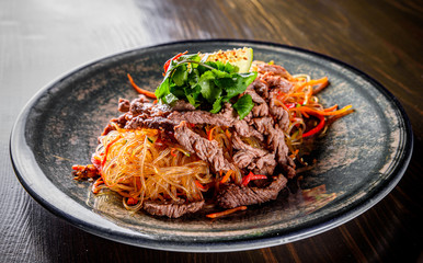Udon stir-fry noodles with beef meat, vegetables and sesame in plate on wooden table background
