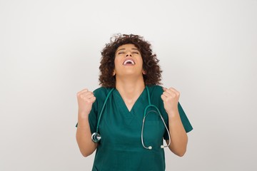 Portrait of beautiful doctor female looks with excitement up, keeps hands raised, notices something unexpected, poses indoors. Lovely woman reacts on sudden news