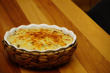 Cauliflower with bechamel sauce and melted cheese on top in ceramic dish with straw mat cover