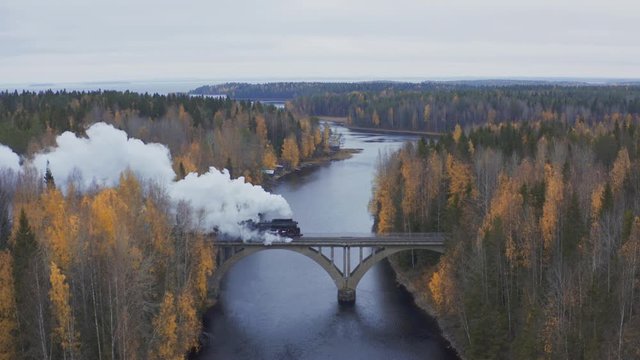 Aerial view steam locomotive goes over the bridge in autumn forest. Retrro steam train ruskeala express