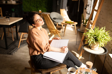 Fototapeta premium young stylish girl with magazine in coffee shop, lifestyle, trends, enjoying sun, drinking coffee next to the window