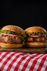 two hamburgers on wooden chopping board on checkered tablecloth isolated on black