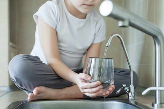 Child is using filter to purify drinking water. Kitchen faucet. Filling cup beverage. Pouring fresh drink. Healthy lifestyle. Quality check. World water monitoring day. Environmental pollution concept