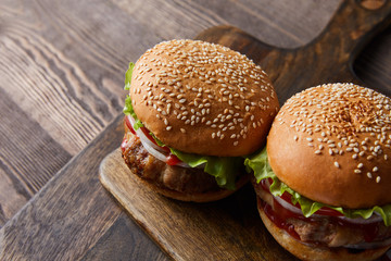high angle view of two burgers on wooden cutting board, cutlery, oil, vinegar and beer bottles isolated on black