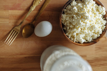.cottage cheese in a wooden cup golden fork and spoon and egg on a wooden board