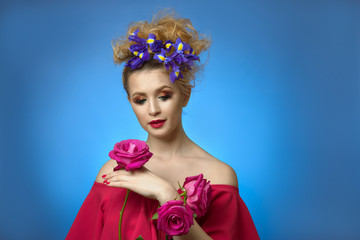 portrait of a cute young girl. beauty make-up. woman holds pink rose in her hands. in the hairstyles of the lady flowers blue iris.