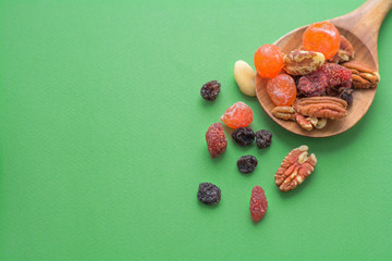 tasty dried fruits and nuts on a wooden spoon and green background