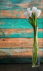Five white tulips stand in a transparent vase on a wooden table and background