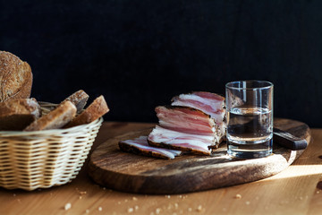 Lard on a cutting board, a glass of vodka and bread on the table.
