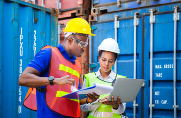 Worker man in hardhat and safety vest holding clipboard checklist and Female foreman using laptop control loading containers box from cargo