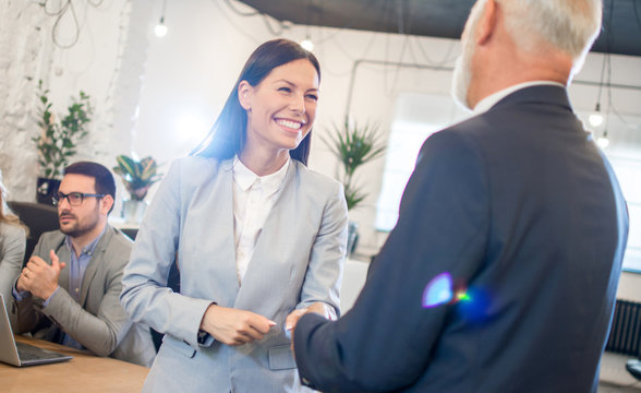 Smiling young businesswoman shaking hands with senior businessman in office