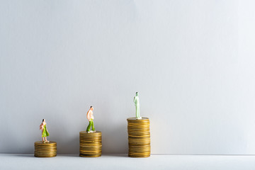 Three people figures on stacked golden coins on white surface on grey background, concept of...