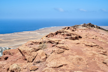 Fototapeta na wymiar Der Vulkan Montana Roja de Playa Blanca mit einer Höhe von 194m und im Hintergrund die Südwestspitze der Atlantikküste auf der Kanareninsel Lanzarote