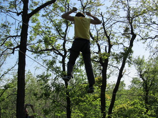 Silhouette of a young man climbing in rope park, man moves on cables and stretched ropes