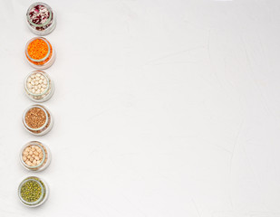 A variety of dry cereals for vegetarians in glass jars: lentils, chickpeas, beans, buckwheat on a white background