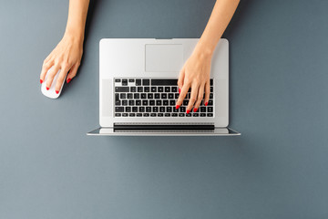 Overhead shot of woman’s hands using laptop on gray table. Office desktop. Flat lay