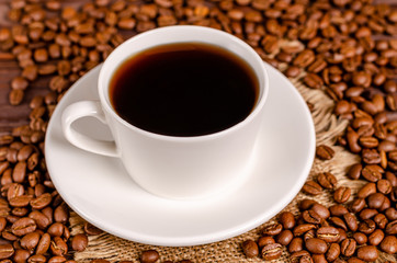 A cup of black aromatic coffee in a white cup on a background of roasted coffee beans arabica coffee on a wooden table