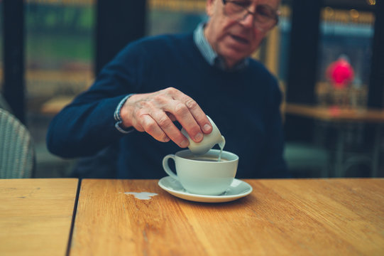 Mature man pouring milk into his coffee and spilling it