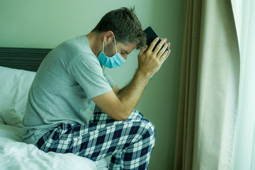 virus outbreak - dramatic portrait of sick man in medical facial mask sitting on bed scared and worried infected by coronavirus suffering lockdown alone at home in quarantine