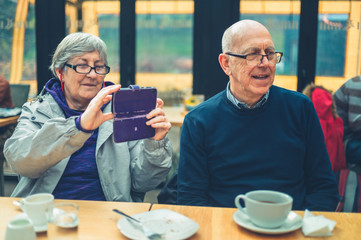Mature woman using smartphone to take pictures with her husband in cafe