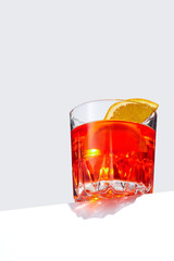 Negroni cocktail is contained in a low crystal glass with orange slices and ice cubes and isolated on a table edge. The showy illustrative picture is made on the gray backdrop.