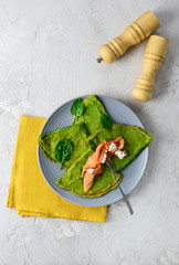 Spinach pancakes with pieces of salmon and curd cheese on a gray plate. Healthy food concept,...