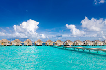 Obraz premium Water villas bungalows and wooden bridge at Tropical beach in the Maldives at summer day