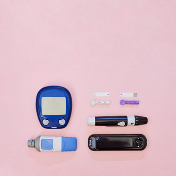 Diabetic kit: two types of glucometers, test strips, lancet. Top view, pink background, empty space.
