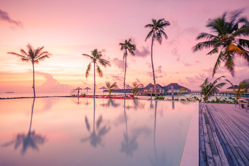 Fototapeta na wymiar Luxury sunset over infinity pool in a summer beachfront hotel resort at tropical landscape. Tranquil beach holiday vacation background mood. Amazing island sunset beach view, palms swimming pool