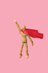 Wooden mannequin miniature doll in a red cape flies up as a superman.