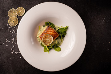 Grilled salmon steak with lemon and herbs, on a white plate, black background. See food. Top view, copy space.