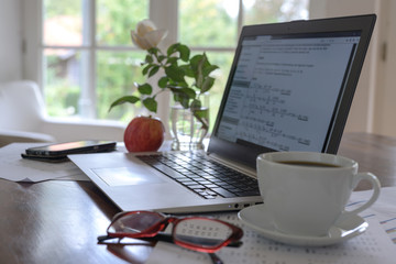 laptop with mathematical formulas on the screen, coffee cup, glasses and a fresh apple on the desk of a student, programmer or a freelancer small business home office