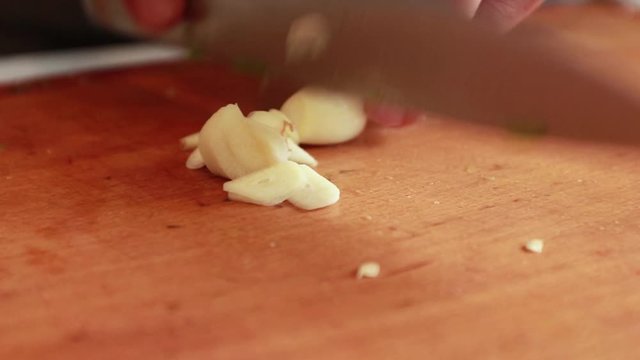 Chef slicing garlic cloves on the cutting board with a knife
