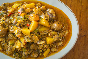 Kerang saus padang is Indonesia food made from mussels, potato,  chili sauce, tomato sauce, garlic and other ingredients. has a savory and spicy taste. in white plate on wooden background