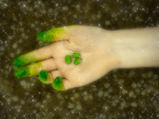 Hand with green fingers holding three green beans surrounded by a soft sparkly haze representing planting seeds during the Spring festival of Ostara