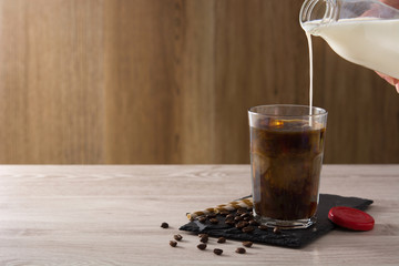 Preparing iced coffee or caffe latte in a tall glass on wooden table. Copy space