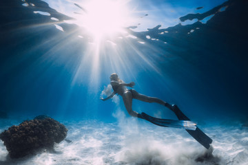 Woman free diver glides with white sand over sandy sea. Freediving underwater in Hawaii