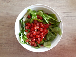 Green salad with small tomatoes in a white bowl on a wooden table