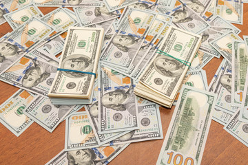 Fototapeta premium Many hundred dollar bills on wooden table background texture. bundles of money scattered on the office desk. wealth and income concept