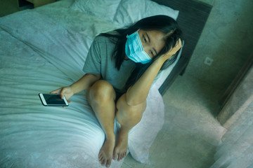 virus outbreak - young beautiful sad and worried Asian Chinese woman wearing medical face mask in quarantine and lockdown at home in panic as prevention vs coronavirus