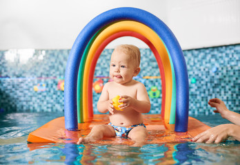 Cute little boy wearing a diaper holding his rubber toy, sitting on a floating colorful construction in the swimming pool. Concept of healthy childhood