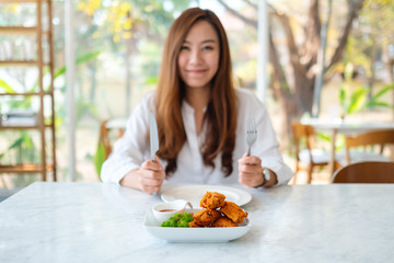 Closeup image of a beautiful asian woman using knife and fork to eat fried chicken in restaurant