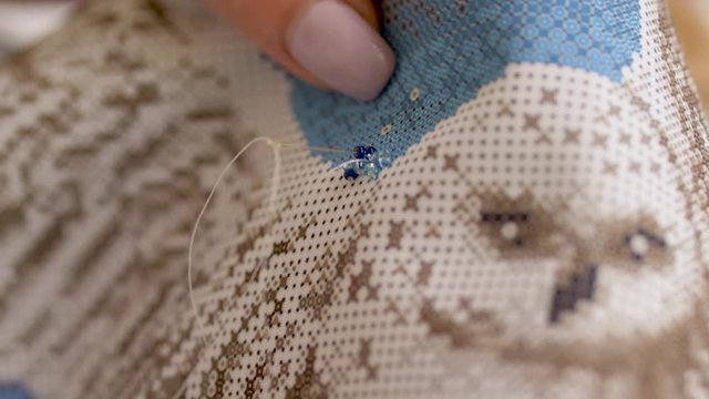 Bead Woman embroidering a picture with an owl. Bead embroidery. closeup