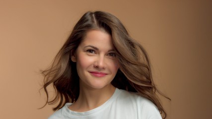 Fototapeta premium Monochrome natural makeup look Caucasian woman in studio in white t-shirtwith healthy shiny hair blowing Happy smiling brunette with blowing hair